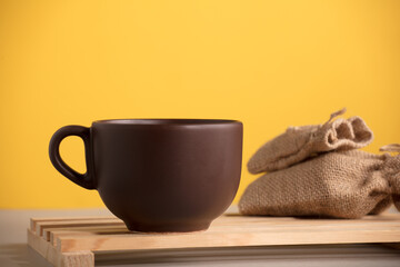 brown cup with coffee or chocolate on wood, with raffia sacks, yellow background