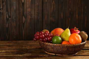 Fresh ripe fruits in wicker bowl on wooden table, space for text