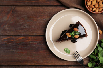 Piece of tasty homemade chocolate cake with mint and almonds on wooden table, flat lay. Space for text