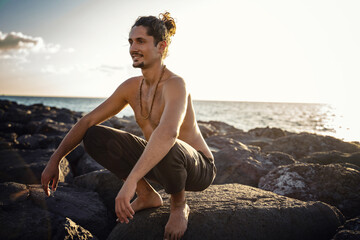 Yoga teacher is practicing on the rocks, sunset time. Man exercising, stretching body. Pranayama....