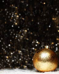 Christmas decorations view of gold evening ball with gold glitter on it on dark background with silver and gold colors bokeh and artificial snow. Holidays concept with copy space at the top