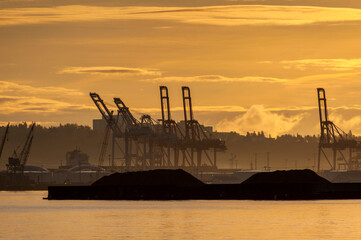 Fototapeta premium Sunrise on Elliott Bay with Silhouetted Seattle Dockyard Cranes. Waterfront with cranes for loading shipping containers onto container ships.