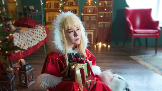Cute girl cosplaying Christmas Miku Santa dress with gifts. New Year's elf. Sits on the floor