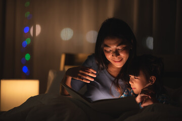 Fototapeta premium young Asian mother and little daughter girl on bed, cozy love sleepy at childhood home, at night
