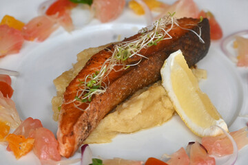 A delicious recipe of fresh cooked salmon steak decorated with fruits and herbs served on a clean white plate.