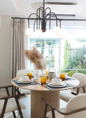 Plate setting on round table in modern style dining room interior of modern home. Dinning room with grass flower and big window.