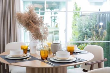 Plate setting on round table in modern style dining room interior of modern home. Dinning room with grass flower and big window.
