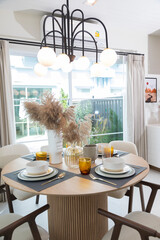 Plate setting on round table in modern style dining room interior of modern home. Dinning room with grass flower and big window.