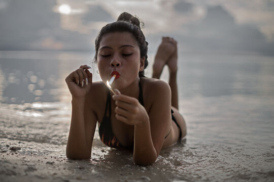 cool pretty young woman lying down smoking a cigarette on the seashore in sunset
