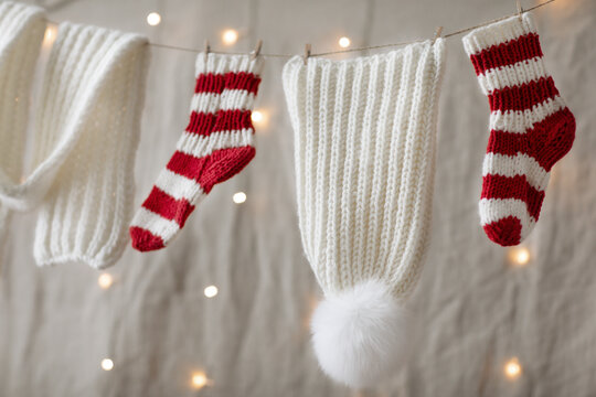Decoration Santa Christmas garland of woolen knitted hand made winter clothes for Santa presents.Lights background.wool knitted striped socks for kid bare feet.
