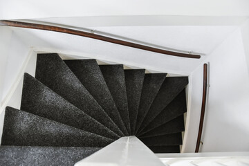 Stylish spiral staircase with black carpet floor and comfortable wooden handrails