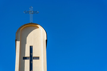 Cross on top of catholic tower church against deep blue sky