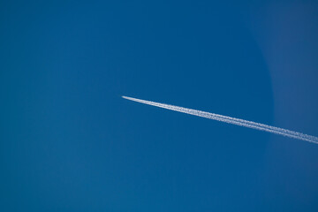 Jet airpllane with thick trace flies to the sun in deep blue sky
