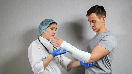 Brunette doctor in medical cap and gloves examines broken spoke bone in gypsum of young...