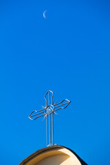Cross on top of catholic tower church against deep blue sky and morning crescent