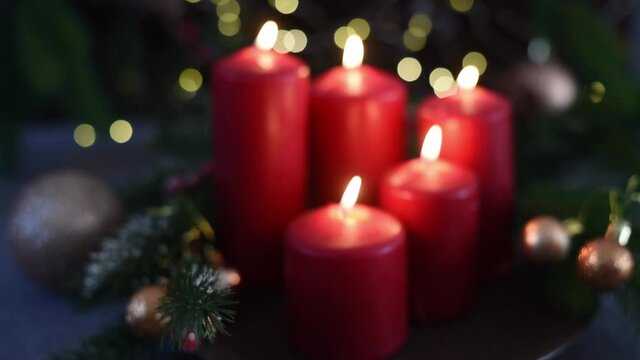 selective focus, blurred Christmas  five red candles lighting, and become focus, spruce branches, cones, balls and garland on dark background. Side view. New year mood, festive concept. 