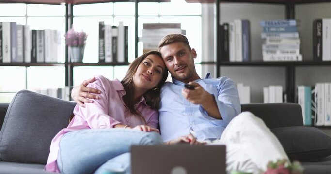 Millennial Caucasian beautiful lovely sweet housewife sitting on cozy sofa massaging her happy husband shoulder and arms while complimenting typing working with laptop computer on table in apartment.