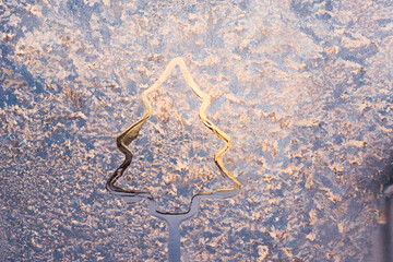 drawing of a fir-tree on an icy winter window. christmas theme. cold winter 2022 patterns on the winter window the glass outside the window is frosty