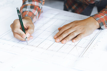 Young technician, engineer, designer holding a pencil drawing on a blueprint on his desk to create a project in the office..And free space to enter your text.