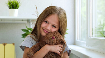 Portrait of a little girl with toy bear looking at camera. Smiling beautiful kid in a bright room...