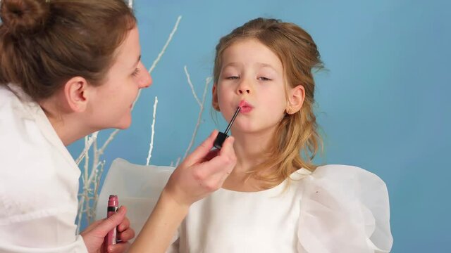 Mom does makeup for her daughter. woman paints lips of a girl. Gloss for baby lips. child on holiday is happy and having fun. Happy family. Young beautiful mother does makeup pretty daughter 