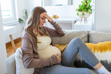 pregnant young adult woman resting on sofa at home, feeling unwell. Young pregnant woman has suffered from headaches sitting on the sofa. Pregnancy symptoms