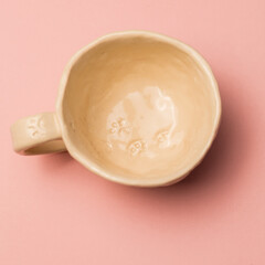 An empty beige handmade clay mug on a pink background, a close-up view from above. A mug decorated with ornaments in the form of cat paws. Fashionable pastel colors