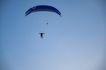 Silhouette of a man on a paraglider flying in the blue sky.