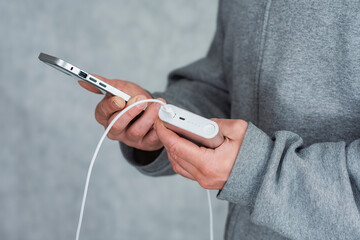 A man holds a power bank in his hands and charges smartphone on a gray background.