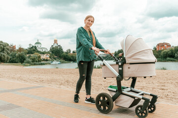 Young woman with baby carriage walk near river
