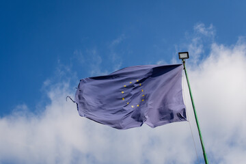 European Union flag blowing in the wind towards cloudy blue sky in a sunny sprng day.