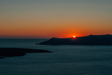 Naklejka na ściany i meble The sun at sunset almost disappeared behind the island, Santorini, Greece