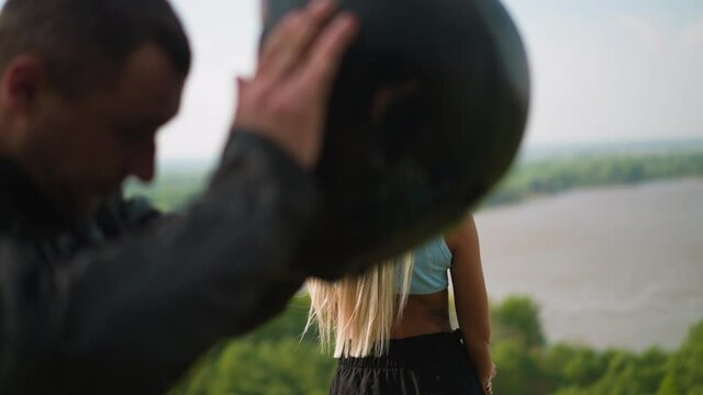 Long blonde haired woman enjoys view of large picturesque river while man biker takes off hardhat on hilly bank on spring day slow motion