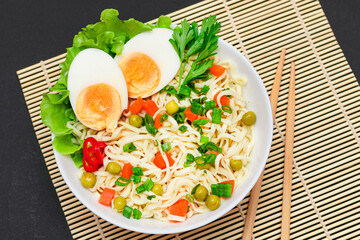 Beautiful Noodle Dish with Green Pea, Carrot, Eggs, Red Hot Pepper and Greens on Sushi Mat. Instant Noodles with Vegetables