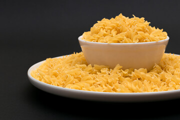 Uncooked Fusilli Pasta Lying on White Plate on Black Background. Raw and Dry Macaroni. Unhealthy and Fat Food