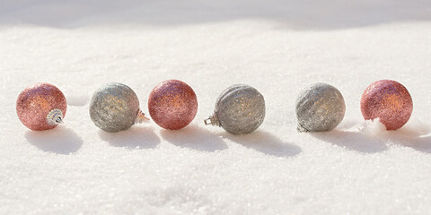 Christmas balls snow. Silver and pink shiny Christmas decorations lie on the snow and sparkle. The concept of a holiday, gifts, congratulations. Horizontal snow banner in bright sunlight. Copy space