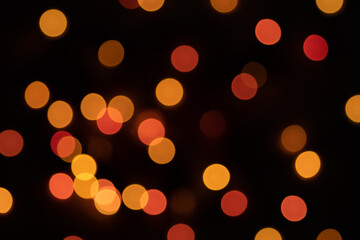 Defocused bokeh lights on black background, an abstract naturally blurred backdrop for Christmas eve or birthday party. Festive light texture. Yellow and red garland in blur. Overlay effect for design