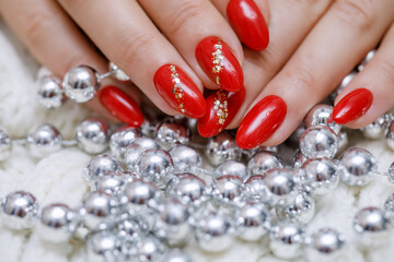 Red manicure with gold decor with silver Christmas tree beads. Hand care in winter. Beautiful feminine hands coated with gel polish. Horizontal photo of hands close-up.