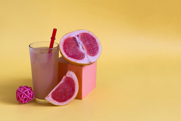 Grapefruit juice and grapefruit slices on a yellow background. Grapefruit juice in a glass glass with a red tube on a yellow background place for text