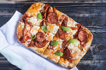Italian pizza with meat, vegetables and herbs on a dark wooden background with a white towel close-up. Fresh pinsa on a wooden background