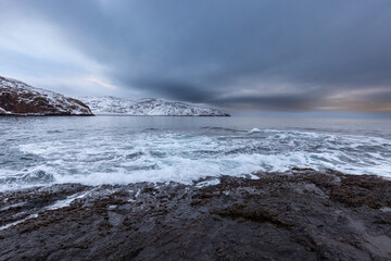 Rolling waves in winter on the rocky coast of the Arctic Ocean. Teriberka village, Murmansk region, Russia.