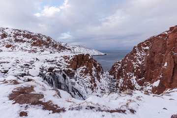 Brown rocks in the snow, view of the northern ocean. Teriberka village, Murmansk region, Russia.