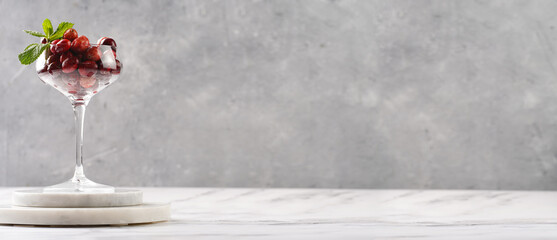 Wide champagne glass filled with fresh raw cranberries on a round marble tray, banner