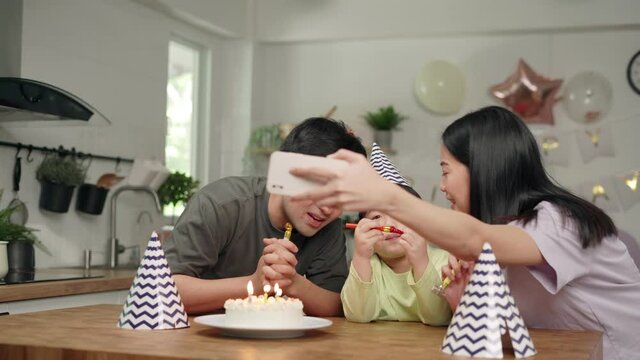 Happy asian family. Father and mother are hosting a birthday party for their son is 5 years old. Father and mother take a picture and live video for grandmother and grandfather on social distance.