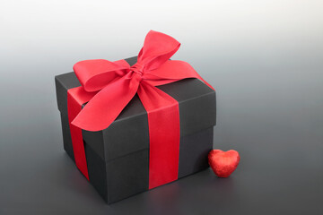 Valentines Day gift box with red bow and heart shaped chocolate   Romantic surprise concept for birthday, anniversary and Christmas. On gradient grey background.