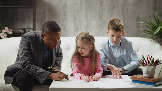 African-American male teacher writes word by finger on table and children try to guess during home lesson with English native speaker slow motion