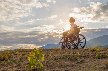 Woman Sitting in wheelchair looking sunset background on mountain.