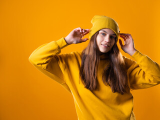 a young cheerful brunette in bright clothes is dancing and having fun. A young woman in a yellow hoodie and a hat on a yellow background