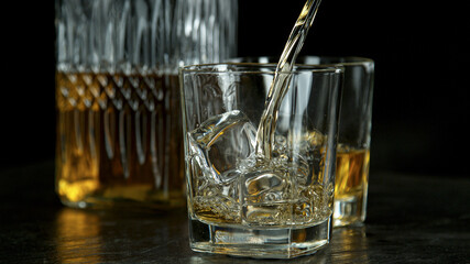 Pouring whiskey into glass on black stone table, freeze motion.