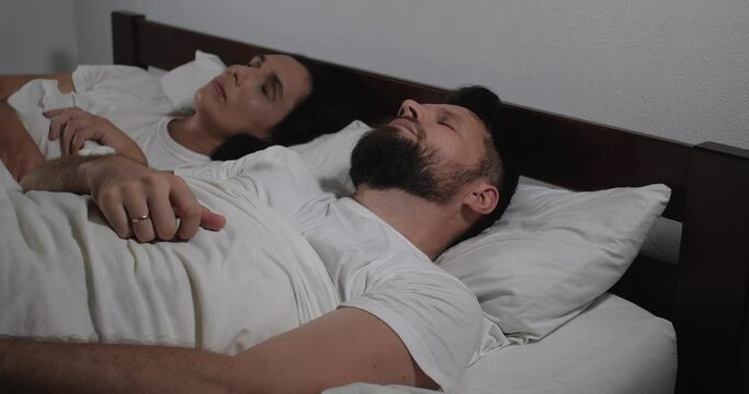 Caucasian couple waking up in bed with white linens in light room. Woman trying to wake up her husband,kissing him and whispering tenderly. Good morning wishing,  calm awakening 4k 